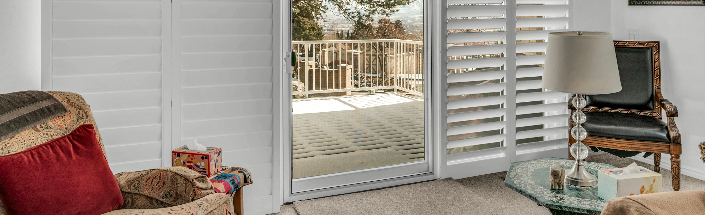 White shutters on a sliding glass door opens to a deck by the ocean.