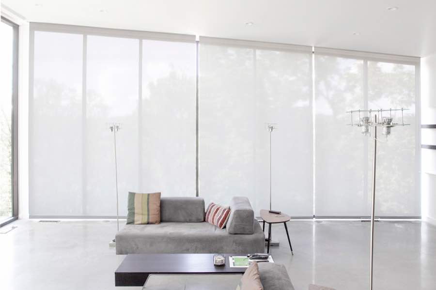 Motorized window shades make controlling natural light effortless in your Dallas great room. White motorized shades on a wall of tall great room windows