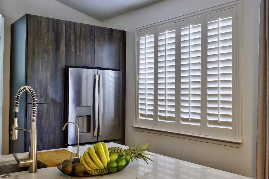 Homeowners use indoor window shutters in Dallas when they want attractive and functional window treatments. Polywood shutters on a large kitchen window