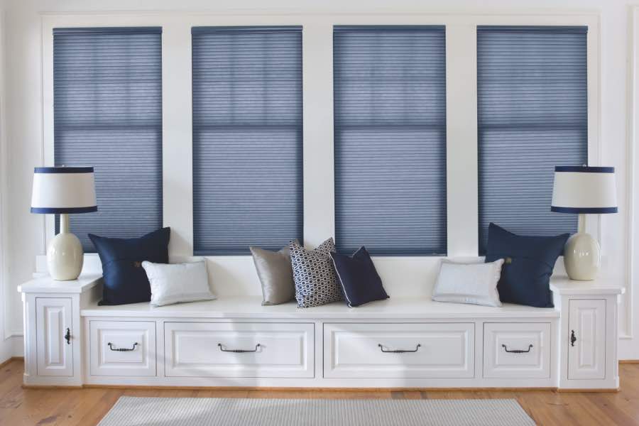Colored window shades look striking against a plain, white wall. Blue cellular shades on four windows over a white window seat