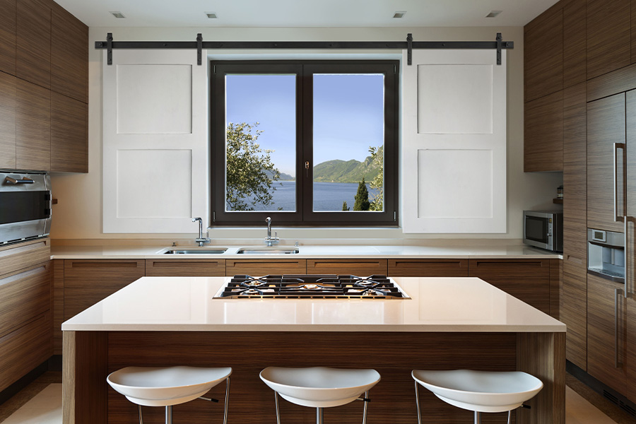 Sliding barn door shutters add class and whimsy to your living space. White farm house style barn door shutters above a kitchen sink.